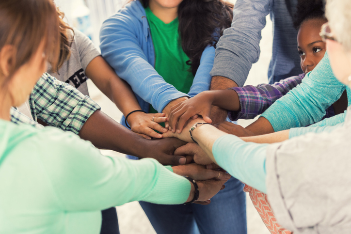 Diverse group of men, women and children put their hands together before starting volunteer project.